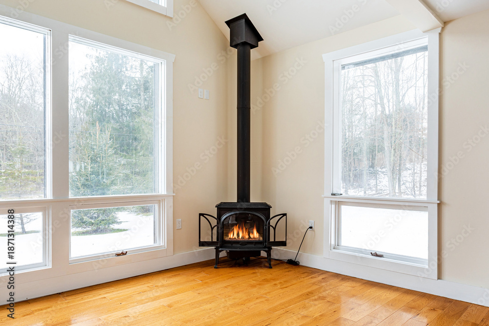 Fototapeta premium Cozy living room with black wood burning stove and large windows, warm minimalist home interior with winter forest view and natural light