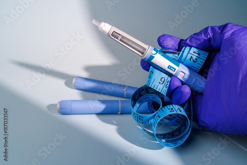 Close up of a gloved hand holding semaglutide GLP-1 pens and blue measuring tape on a blue gradient background for medical weight management.