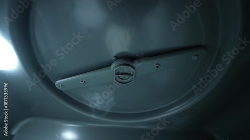 Inside view of dishwasher with mugs, cups, and plates arranged on metal rack. Soft internal light highlights textures. Dark background, focused on dishware and structure.
