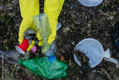 Canvas Print volunteer cleaning polluted beach, collecting plastic bottles, cups and debris in a black bag, supporting ecology, environment protection, sustainability and coastal cleanup awareness