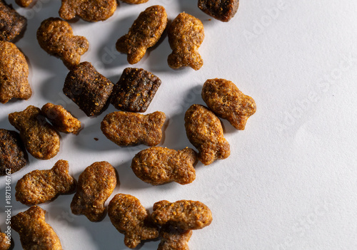 Dry cat food pellets in fish shape on white background macro. Copy Space. Top view macro photography of crunchy fish-shaped dry pet food scattered on a white surface. 