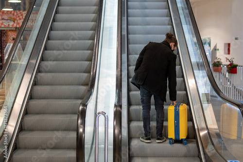 Man with face mask at the airport with a rolling suitcase on escalator