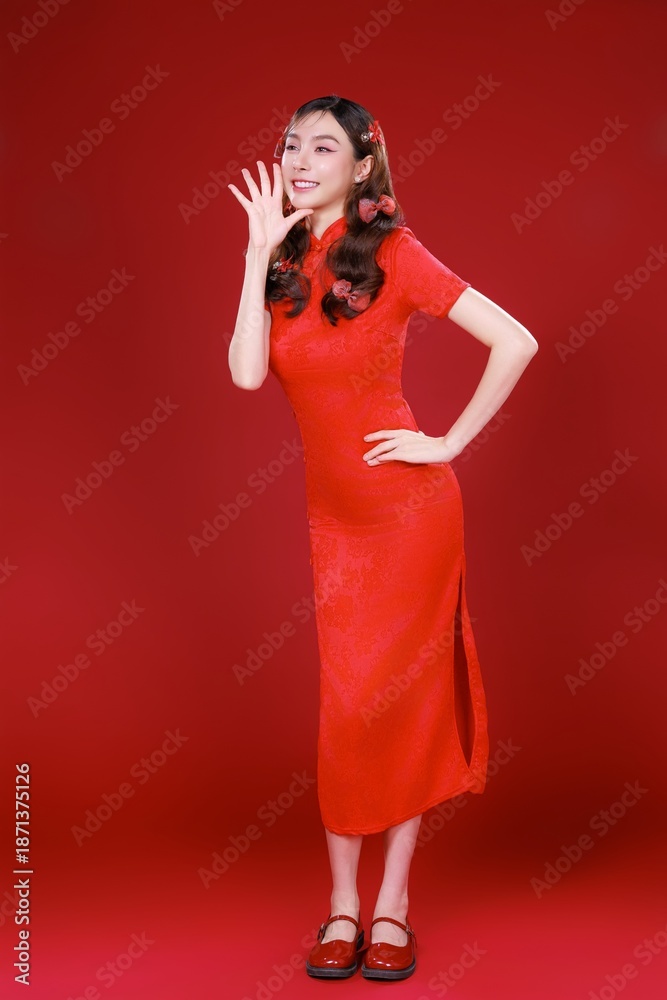 Naklejka premium Mysterious Asian woman in a red Qipao holding a red fan beautiful face against a red background.