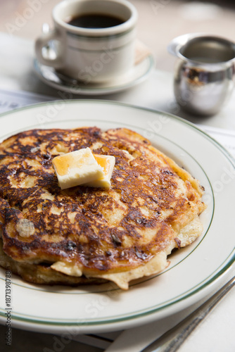 Pancakes with warm maple syrup and butter on a white plate in a restaurant setting.
