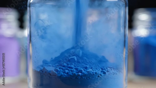 Close Up Macro Shot Of Vibrant Blue Powder Being Poured Into A Glass Jar With Other Colored Powders In Blurry Background Soft Light Creates Atmospheric Effect