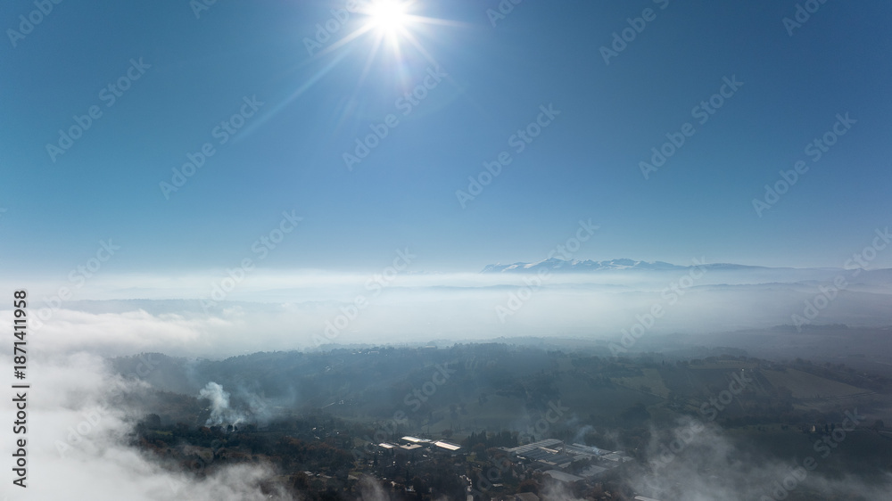 Fototapeta premium Aerial drone photograph revealing a stunning landscape of rolling hills and cultivated fields in the Marche region of Italy, partially covered by soft morning fog.