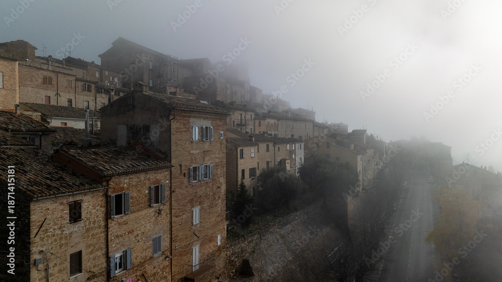 Fototapeta premium Dense fog covering historic town buildings. Moody aerial view, low visibility creates dramatic and cinematic atmosphere.