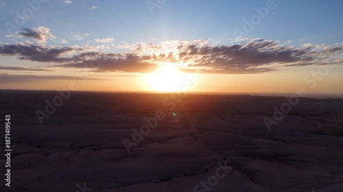 Sun flare sunrise over barren expanse with radiant rays backlighting cracked ground dramatic lens glow warm golden tones and calm