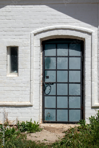 The entrance to the building's utility room is made of white-painted brick. The door has a metal frame and, with its numerous square sections, resembles French doors.