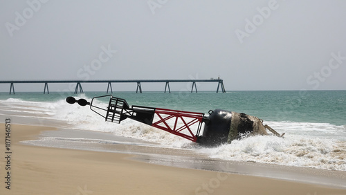 Grande bouée de navigation maritime rouge et noire échouée sur une plage de sable