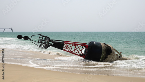 Grande bouée de navigation maritime rouge et noire échouée sur une plage de sable