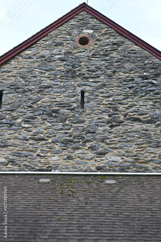 Traditional Stone Gable End of a Historic Rural Building with Weathered Slate Masonry, Small Vent Openings, and Moss-Dotted Shingle Roof Beneath an Overcast Sky