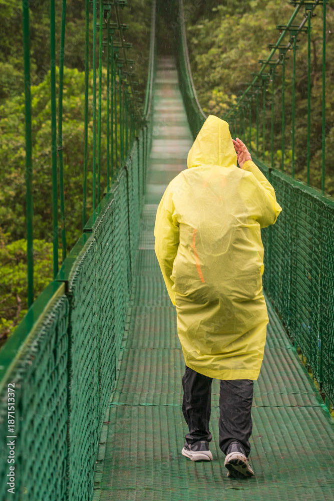 Fototapeta premium Rain soaked tourist crossing the moss and tree filled valley on hanging bridge in rainforest of Monteverde in Costa Rica