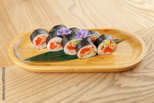 Savory sushi rolls served on a wooden plate with decorative flowers and leaves in a light setting