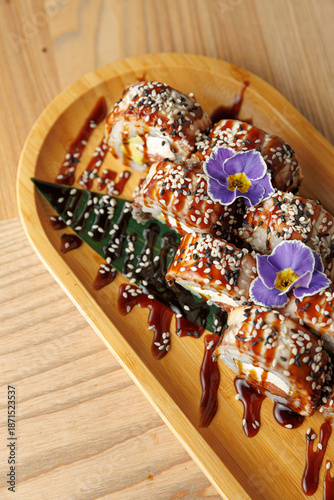 Delicious sushi rolls topped with sesame seeds and flowers served on a wooden platter with sauce
