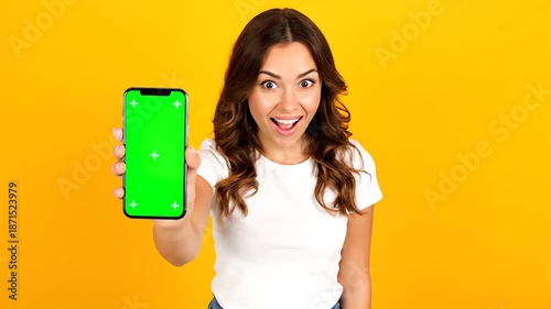 Excited brunette woman displaying a blank green screen Phone Mockup on a smartphone, perfect for your app advertisement or digital content