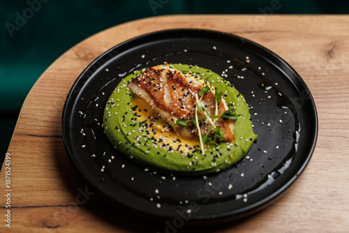 Fusion dish featuring grilled fish atop green puree with sesame seeds, served in a modern restaurant setting