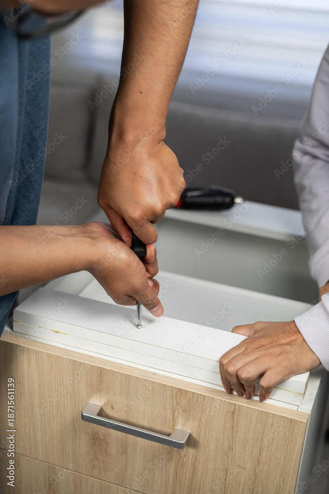 Obraz premium Close up of two people working together to assemble wooden furniture, using an electric drill to secure screws on a flat surface indoors.