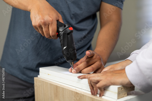 Konstfotografi Close up of a furniture assembly process where two people secure wooden panels together using an electric drill indoors