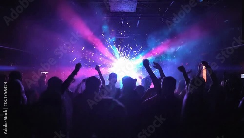 A dark concert scene with a vibrant light burst; silhouettes of an energetic crowd raise hands up!!!