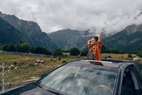 Foto Person standing through the sunroof of a car in a dramatic mountain landscape, celebrating travel outdoors with a joyful expression, capturing adventure and freedom during a roadside vacation