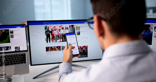 Tableau sur toile Man Reading Multiple Online News Articles On Mobile Phone And Laptop