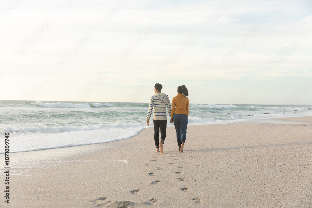 Fototapeta premium Full length rear view of couple walking while leaving footprints on sand at beach