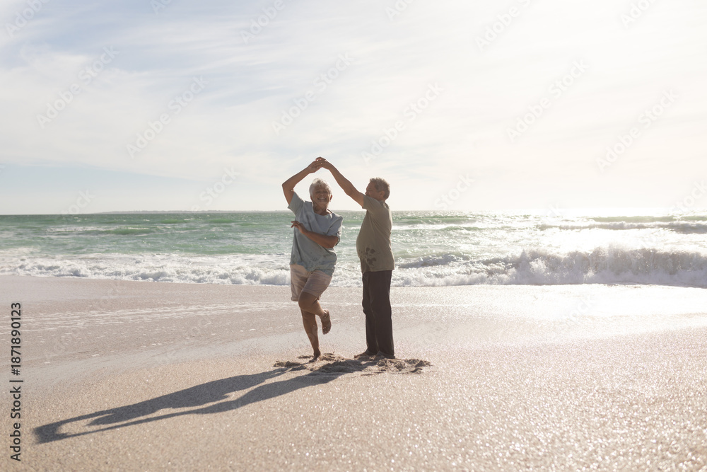 Obraz premium Full length of happy retired senior multiracial couple dancing on shore at beach during sunny day