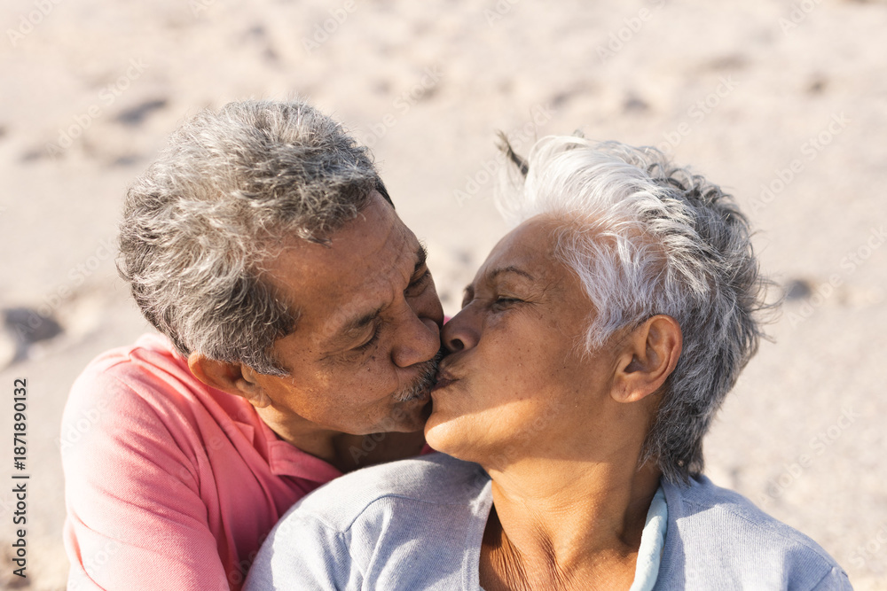 Obraz premium Affectionate multiracial senior couple kissing on lips while enjoying sunny day at beach
