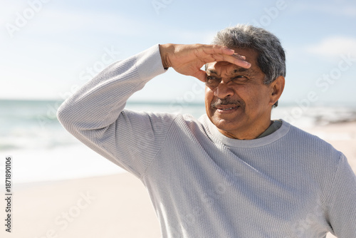 Obraz na plátne Retired senior man shielding eyes while looking away at beach during sunny day