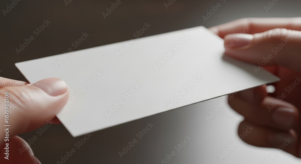 Obraz premium Professional hands presenting a blank white textured business card mockup template on a dark background, ideal for corporate branding identity showcase.