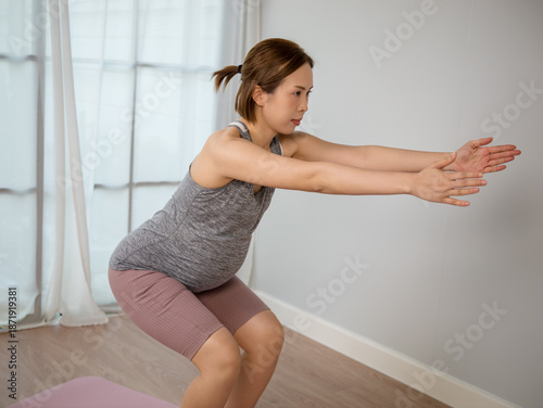 Asian pregnant woman in sportswear doing exercise in living room at home.