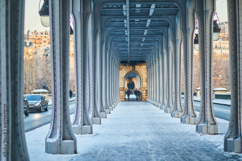 Fototapeta premium Perspective view of the Bir-Hakeim bridge in Paris during winter, with snow covering the walkway and people walking in the distance. Iconic Parisian architecture and cold season atmosphere