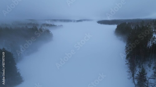 Slow aerial push forward over foggy frozen lake in winter