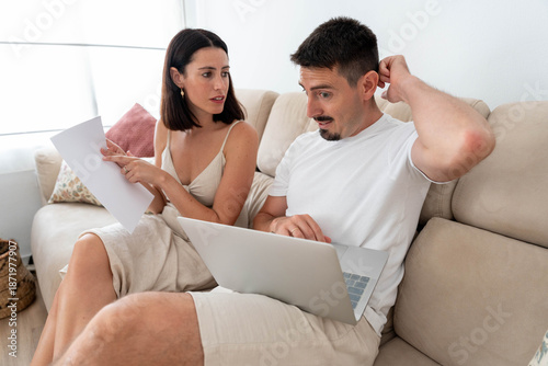 Принти на полотні Young couple on a sofa at home reviewing bills and laptop, looking worried and s