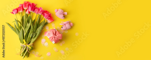 Pair of small baby girl socks, bouquet of pink tulips and gift box on yellow background with copy space for your warm message, baby shower, first newborn party background, copy space