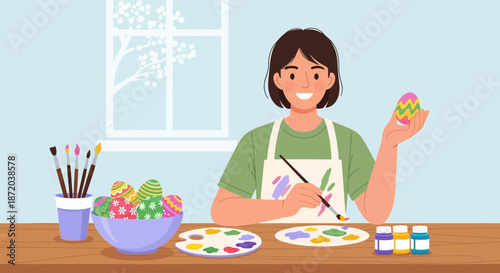 A smiling woman creatively paints vibrant easter eggs at home near a bright window