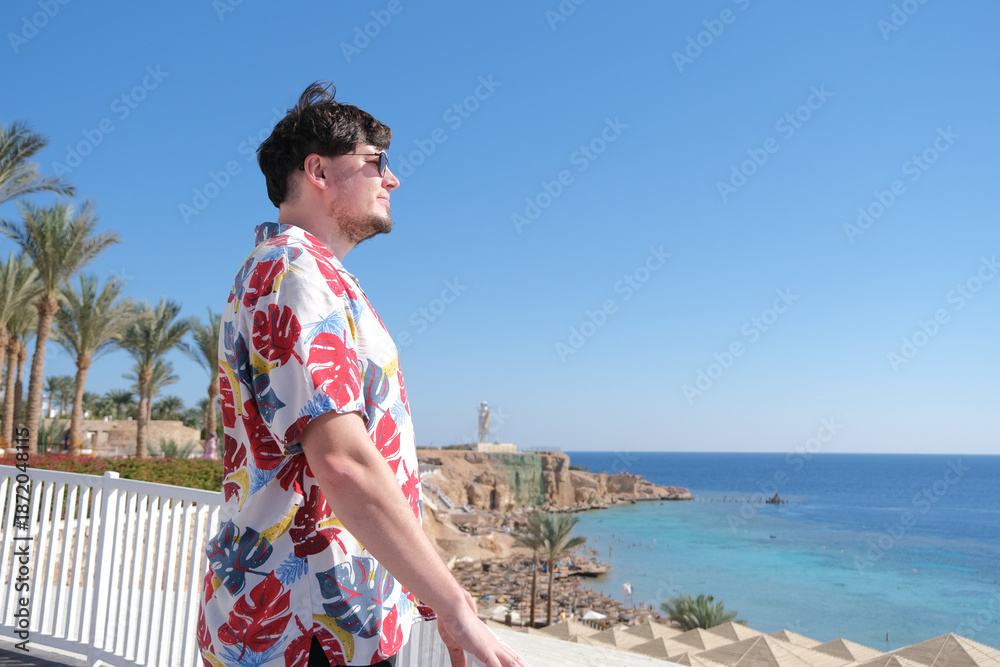Fototapeta premium young man in Hawaiian shirt standing on terrace overlooking red sea, Egypt