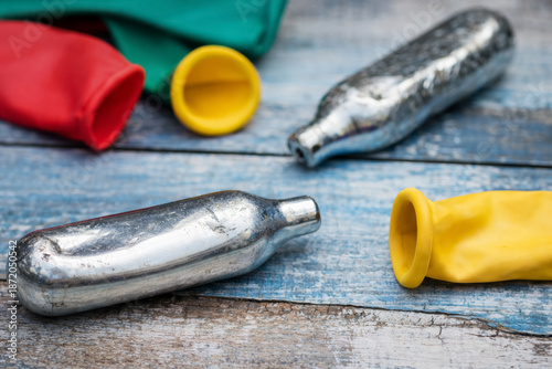 Nitrous oxide cartridges with deflated balloons on wooden table, substance abuse and waste concept