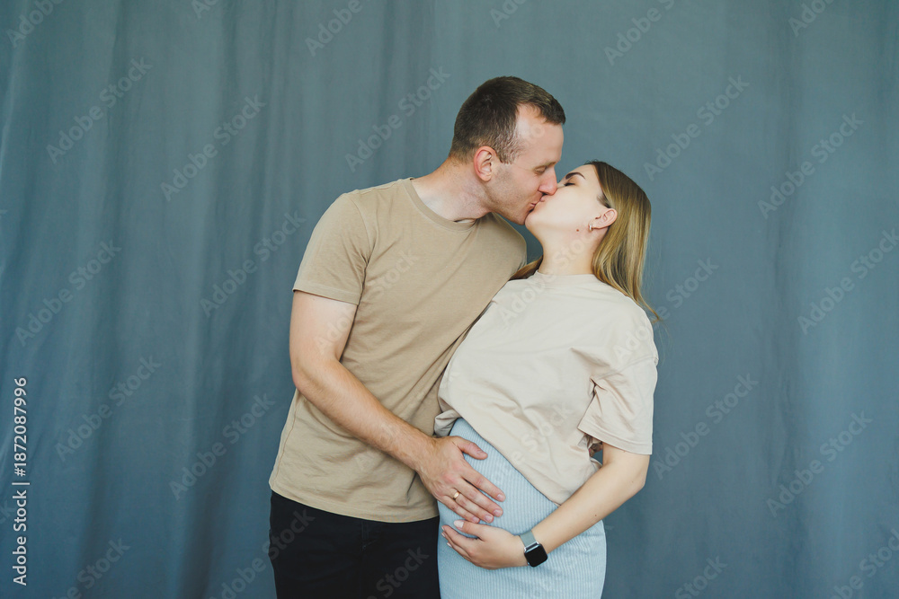 Fototapeta premium Couple shares a moment of love and connection as they prepare for parenthood in a simple indoor setting with a blue backdrop