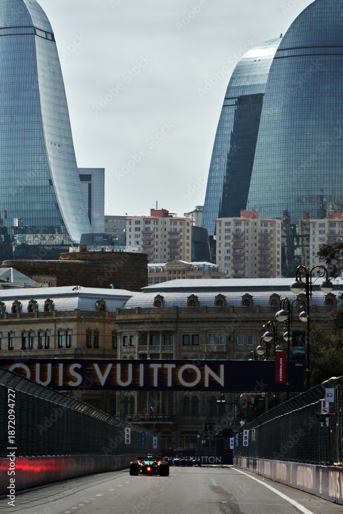 Fototapeta premium BAKU, AZERBAIJAN - SEPTEMBER 19, 2025: A Formula 1 car competes during the Azerbaijan Grand Prix at the Baku City Circuit. The iconic Flame Towers and a large Louis Vuitton sponsorship banner