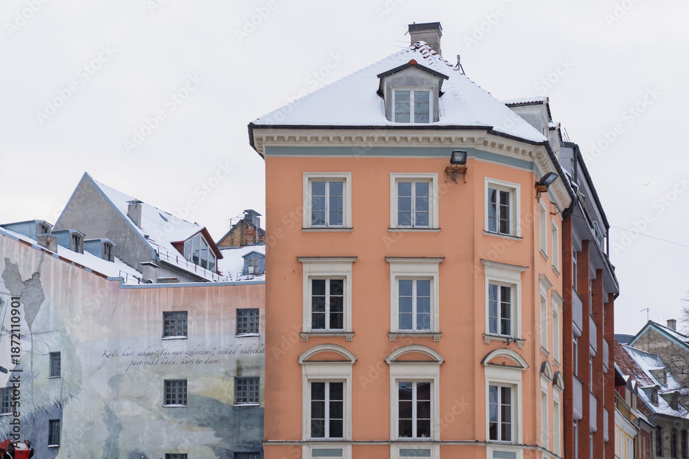 Fototapeta premium Historic Old Town Riga apartment building with orange facade white window frames and snow topped roof representing preserved urban architecture and winter city environment