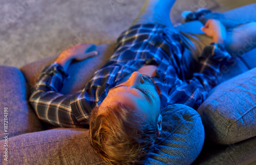 Εκτύπωση καμβά Tired drug addict in depression, overdose and despair lying on living room sofa in neon LED light, top view