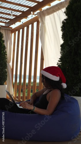 A woman wearing a Santa hat while working on her laptop outdoors