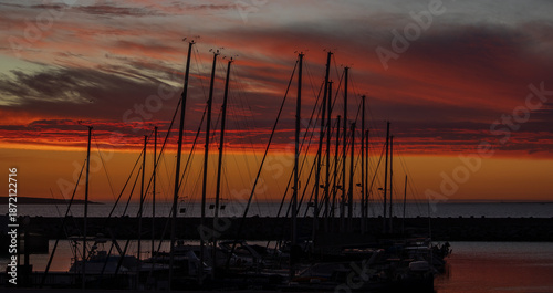 A couple of yachts in the harbor with the silhouette of their masts against a beautiful sunset sky