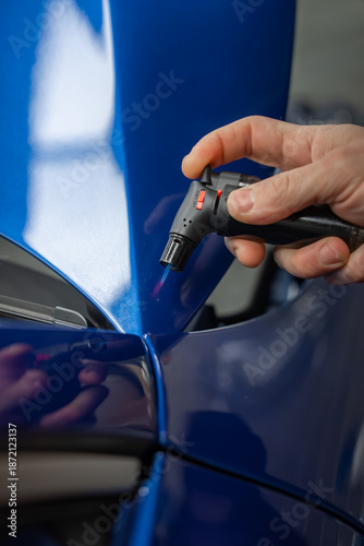 Canvas Print A technician uses a small heat gun on a glossy blue car hood near a panel gap in a dealer workshop