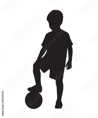 Silhouette of a young boy standing with one foot on a soccer ball, ready to play.