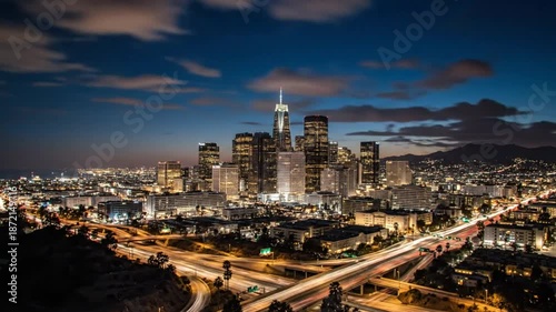 Time-lapse of the Los Angeles skyline transitioning from sunset to night with illuminated city lights and clouds