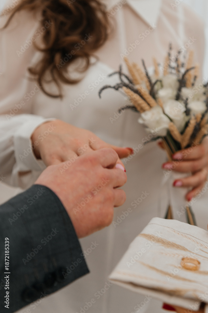 Obraz premium Close-up of bride and groom holding a rustic wedding bouquet. Newlywed couple embracing: Hands, rings, and white flowers. Romantic details: Hands and rings over a bouquet of roses and wheat