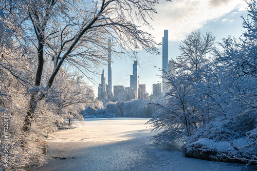 Winter view of Central Park in New York City, with a frozen lake, snow-covered trees, and Midtown Manhattan Billionaires Row skyscrapers